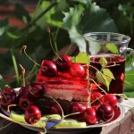 Refrigerio vital entre rojos y verdes:plato con cerezas, tarta de nata y fresa, infusión de frutos rojos. Fondo de grandes hojas verdes (Fuente: Pixabay.com)