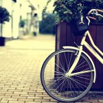 Bicicleta apoyada sobre gran maceta de madera en calle desierta y adoquinada