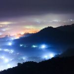 Ciudad iluminada entre la niebla, vista desde la montaña