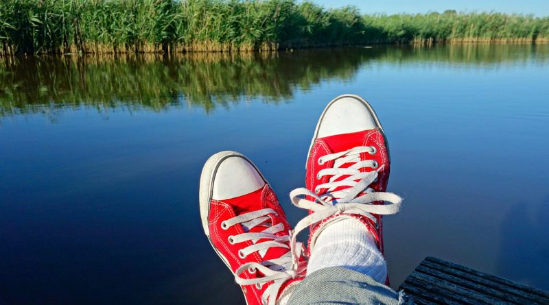 Zapatillas rojas. Pies cruzados contemplando los juncos sobre el agua